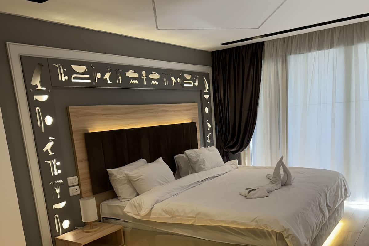A modern bedroom with a large bed, a bedside table, and a wall with illuminated icons.