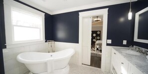 A bathroom with a freestanding bathtub, a large mirror, and a vanity with a marble countertop.