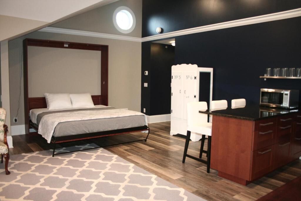 Un dormitorio con una cama, un escritorio, una silla, un microondas y una pequeña kitchenette.