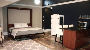 Un dormitorio con una cama, un escritorio, una silla, un microondas y una pequeña kitchenette.