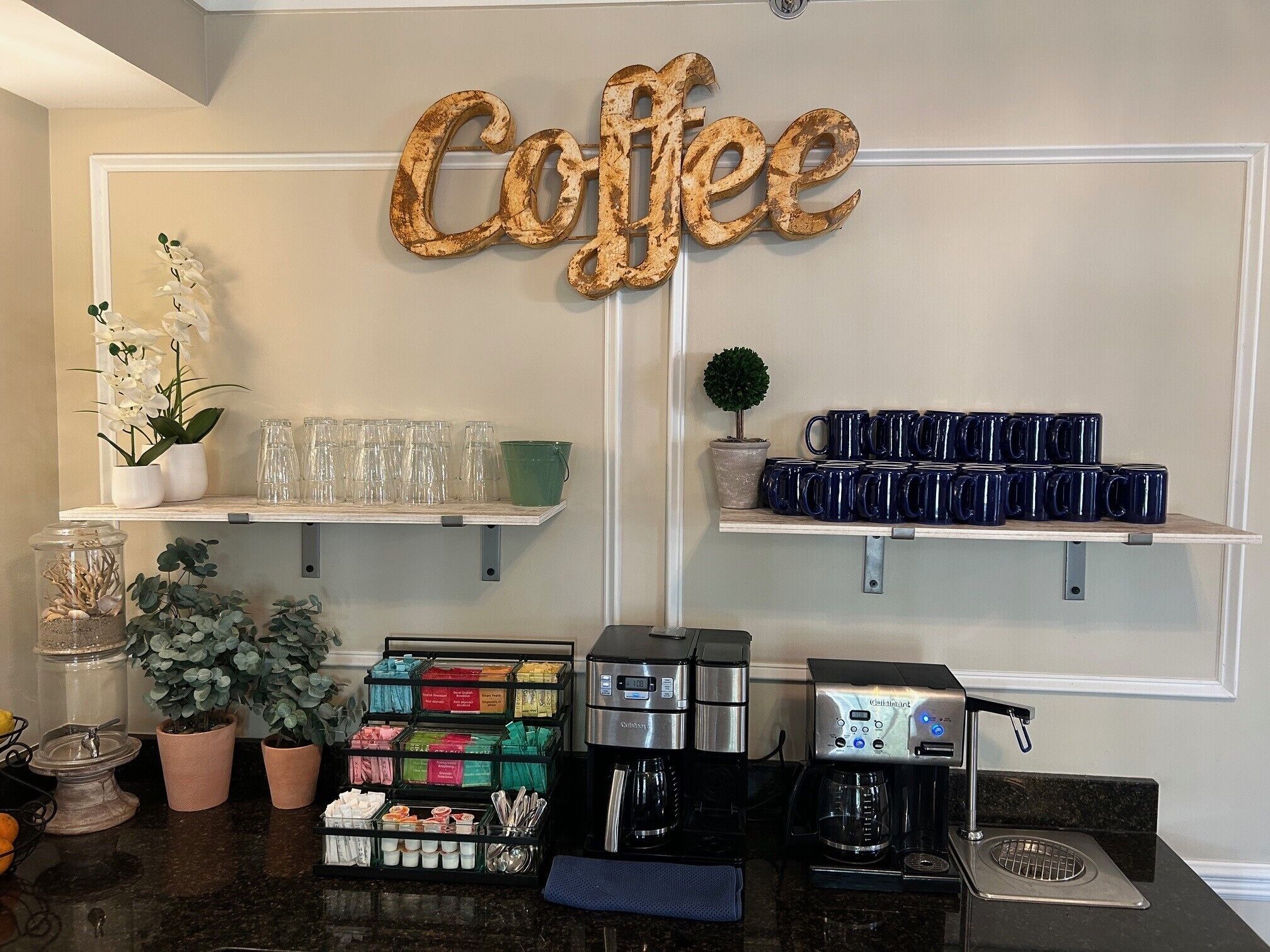 A coffee station with a 'Coffee' sign, glassware, mugs, and coffee machines.