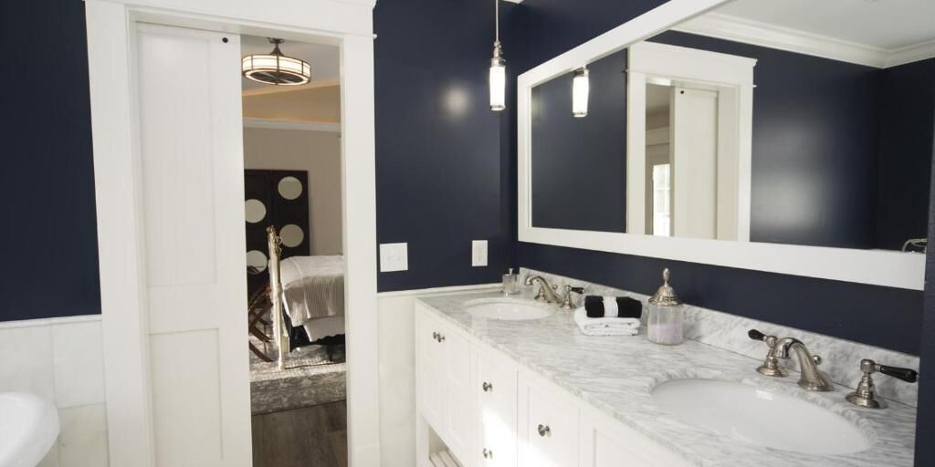 A bathroom with two sinks, a large mirror, and a door leading to another room.