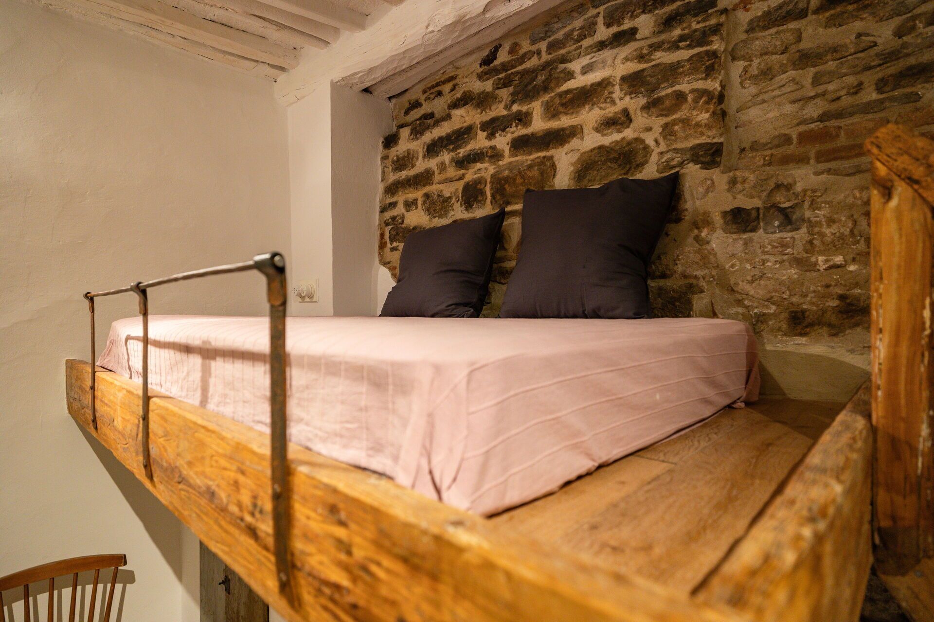 A rustic wooden bed with a metal frame in a room with exposed stone walls.