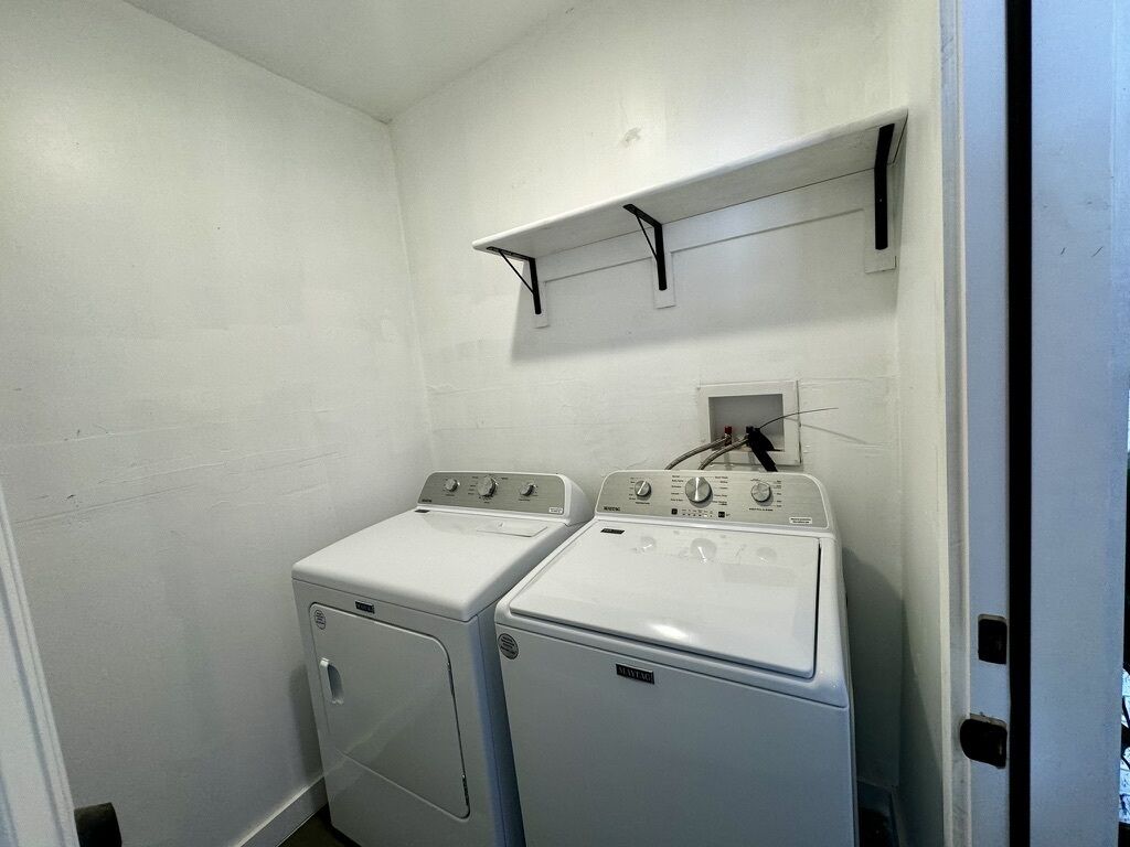 A laundry room with two white front-loading washing machines, a white wall, and a shelf above the machines.