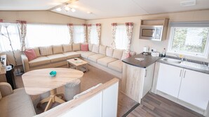 Un intérieur de camping-car compact comprenant un coin cuisine, un espace repas et un coin salon avec un canapé et une table.