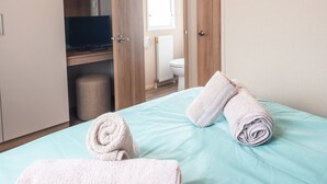 Une chambre avec un lit, deux serviettes enroulées, un bureau avec un ordinateur et une fenêtre.
