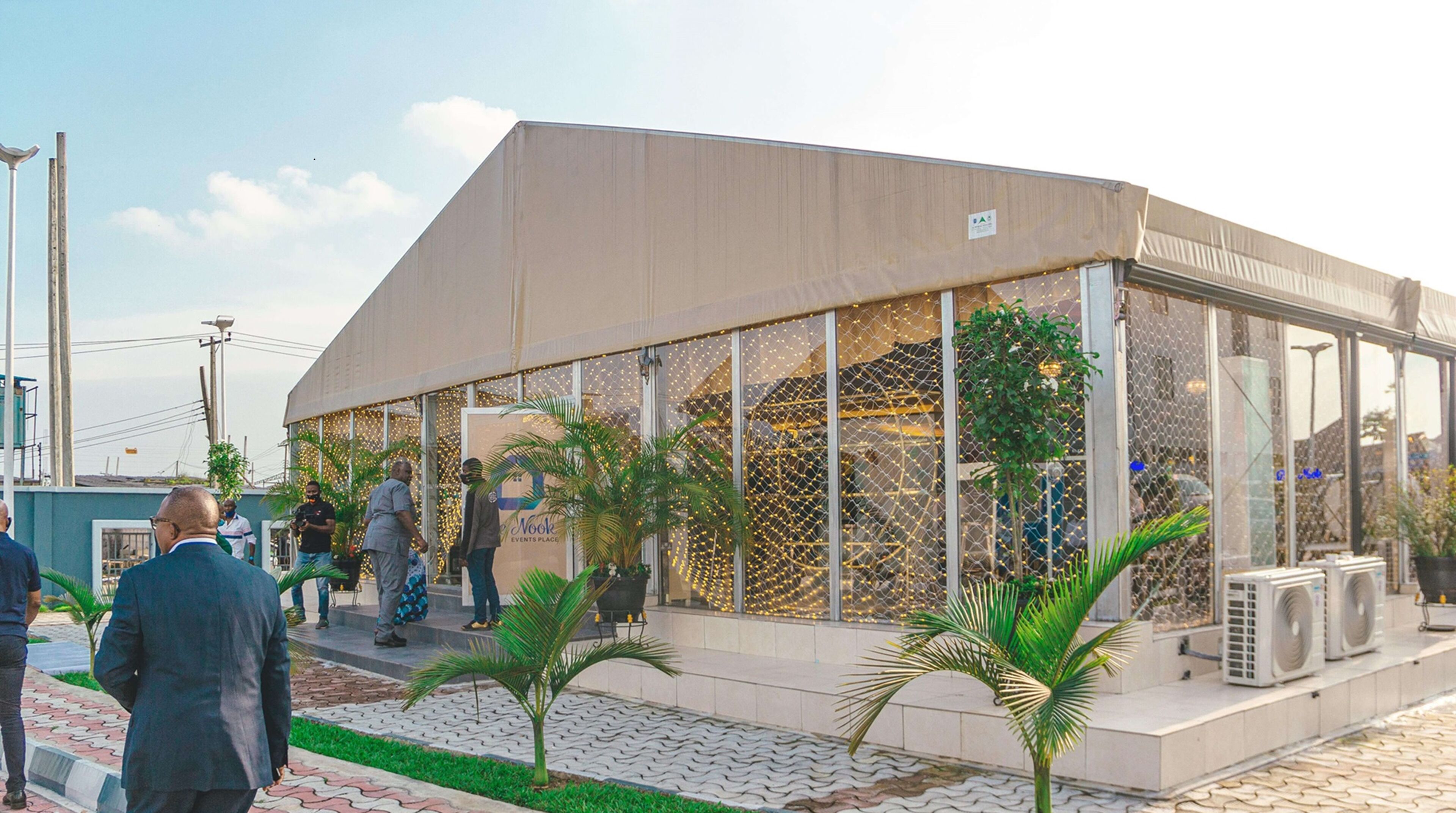 A modern building with large windows and a flat roof, surrounded by a paved area with palm trees.