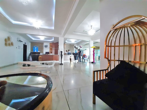 A spacious lobby with a reception desk, a black leather sofa, and a decorative metal cage. - The Nook Apartments (Port Harcourt)