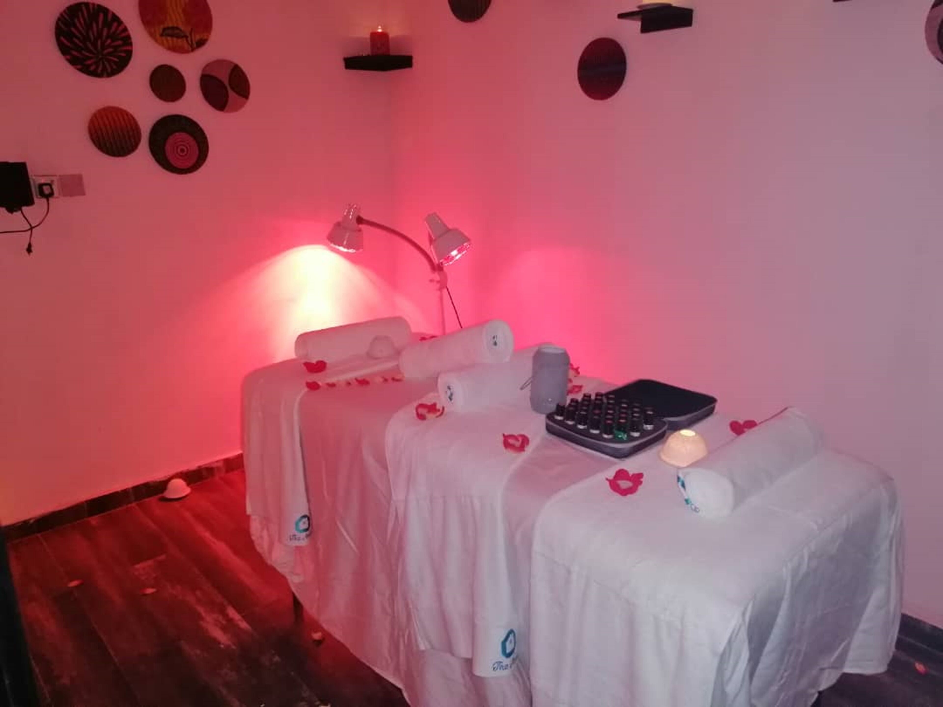 A room with a massage table covered in white sheets, a small table with a keyboard and a candle, and a wall decorated with circular art pieces.