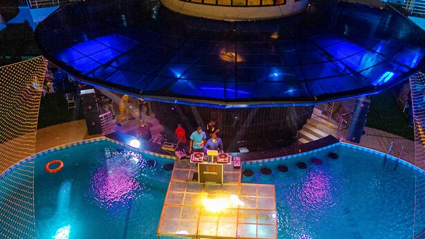 Un área de piscina con cabina de DJ y techo de cristal.