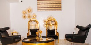 A modern living room with two black leather chairs, a round gold and black coffee table, and decorative wall art. - The Nook Apartments (Port Harcourt)