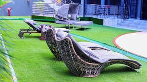 Zona junto a la piscina con sillones de descanso, un espacio de estar cubierto y una escalera que lleva a un nivel superior.