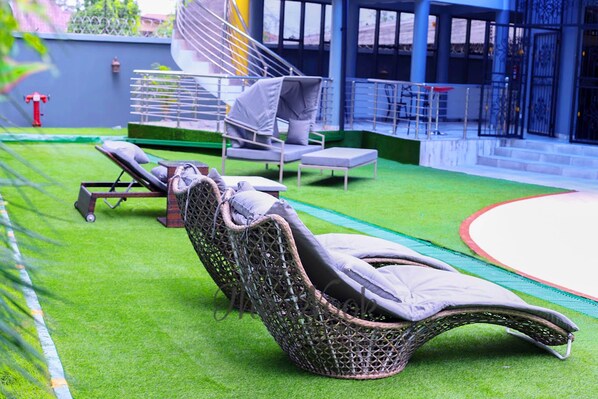 A poolside area with lounge chairs, a covered seating area, and a staircase leading to an upper level. - The Nook Apartments (Port Harcourt)