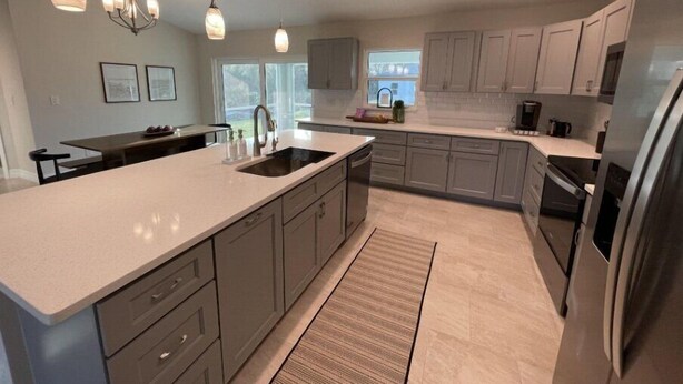 A modern kitchen with a large island, grey cabinetry, stainless steel appliances, pendant lighting, and a view of the outdoors. - Charming, Modern, Cozy Retreat (North Port)