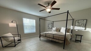 A bedroom with a four-poster bed, a standing lamp, a small table, and artwork on the walls. - Charming, Modern, Cozy Retreat (North Port)
