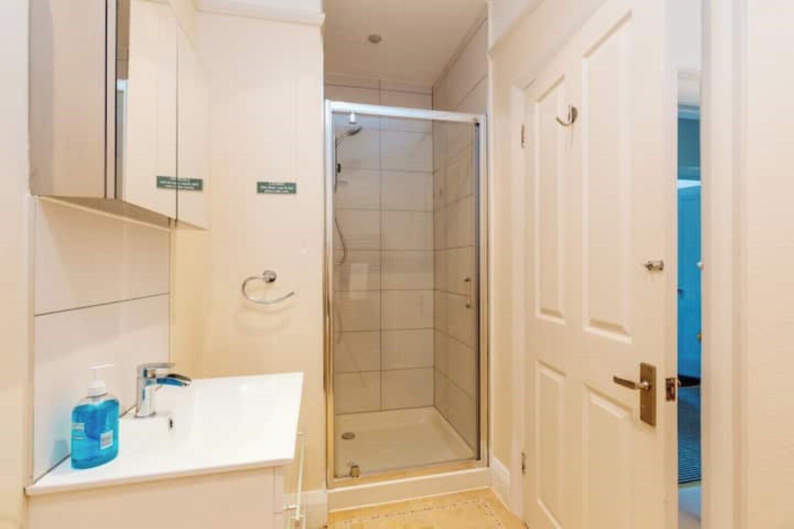 A bathroom with a white sink, a glass shower enclosure, and a door leading to a blue room.