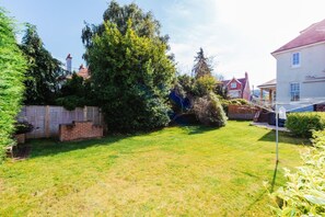 A residential backyard with a grassy lawn, a wooden fence, and a large tree. - Westholme Lodge - Exquisite house with a hot tub. (Minehead)