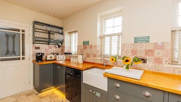 A kitchen with a wooden countertop, a dishwasher, and a sink. There are two windows with blinds, and a sign on the wall.