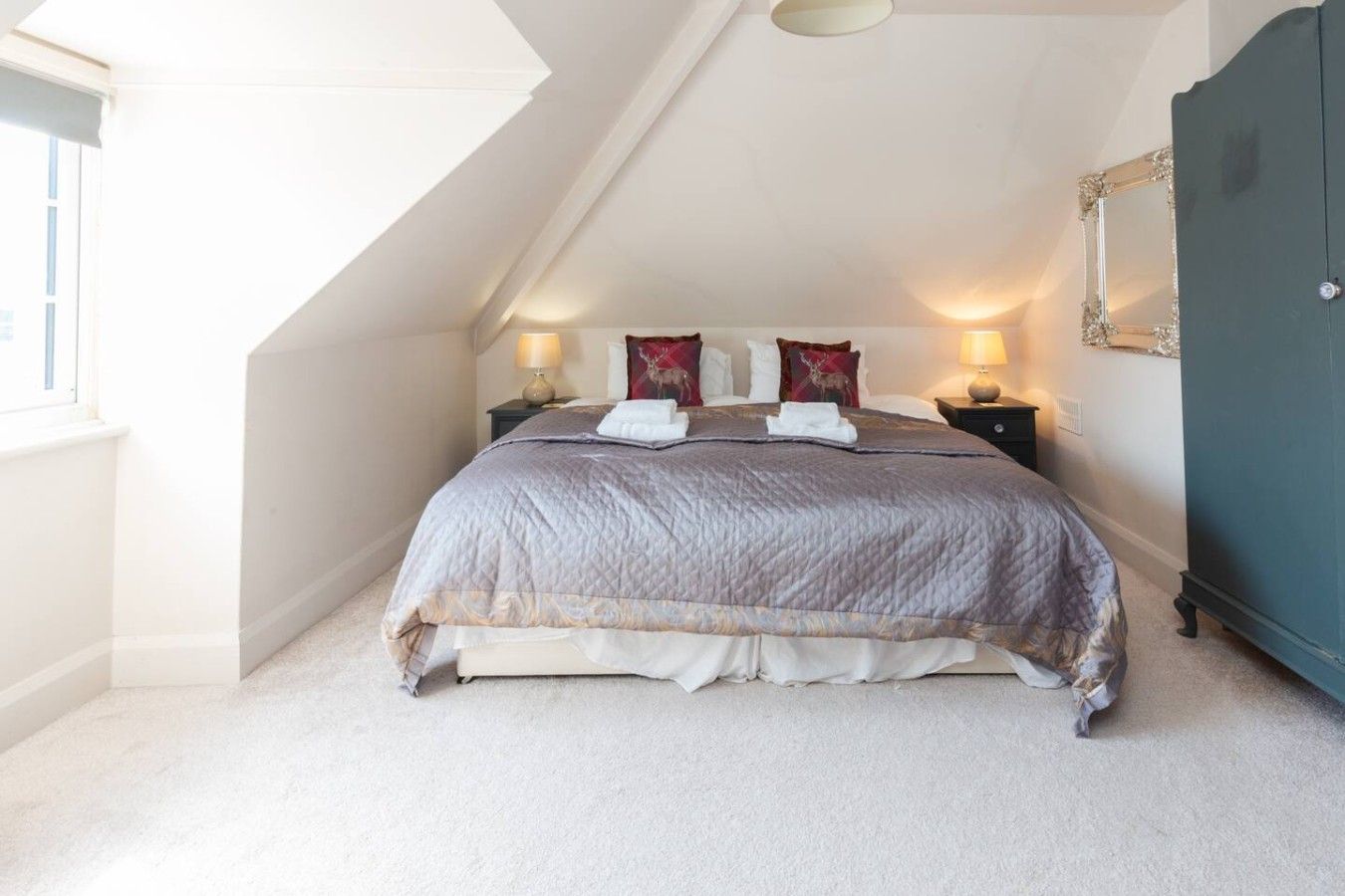A bedroom with a sloped ceiling, a bed with a quilted cover, two bedside lamps, and a mirror on the wall.