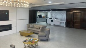 Eine moderne Lobby mit einer Rezeption, einer Sitzecke inklusive Sofa und Sesseln, einem Couchtisch und einer Kristallleuchter.