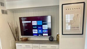 Un salon avec un téléviseur à écran plat fixé au mur, une œuvre d’art encadrée au-dessus, et un meuble blanc en dessous.