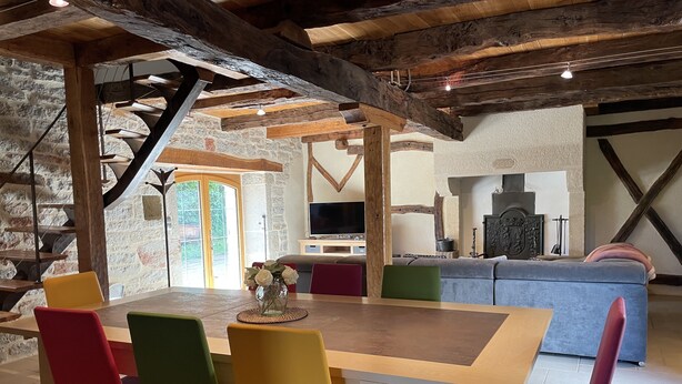 A rustic dining area with a wooden table and colorful chairs, a stone wall, and a staircase leading to an upper level. - le Gite de Cayla (SAINT-PROJET)