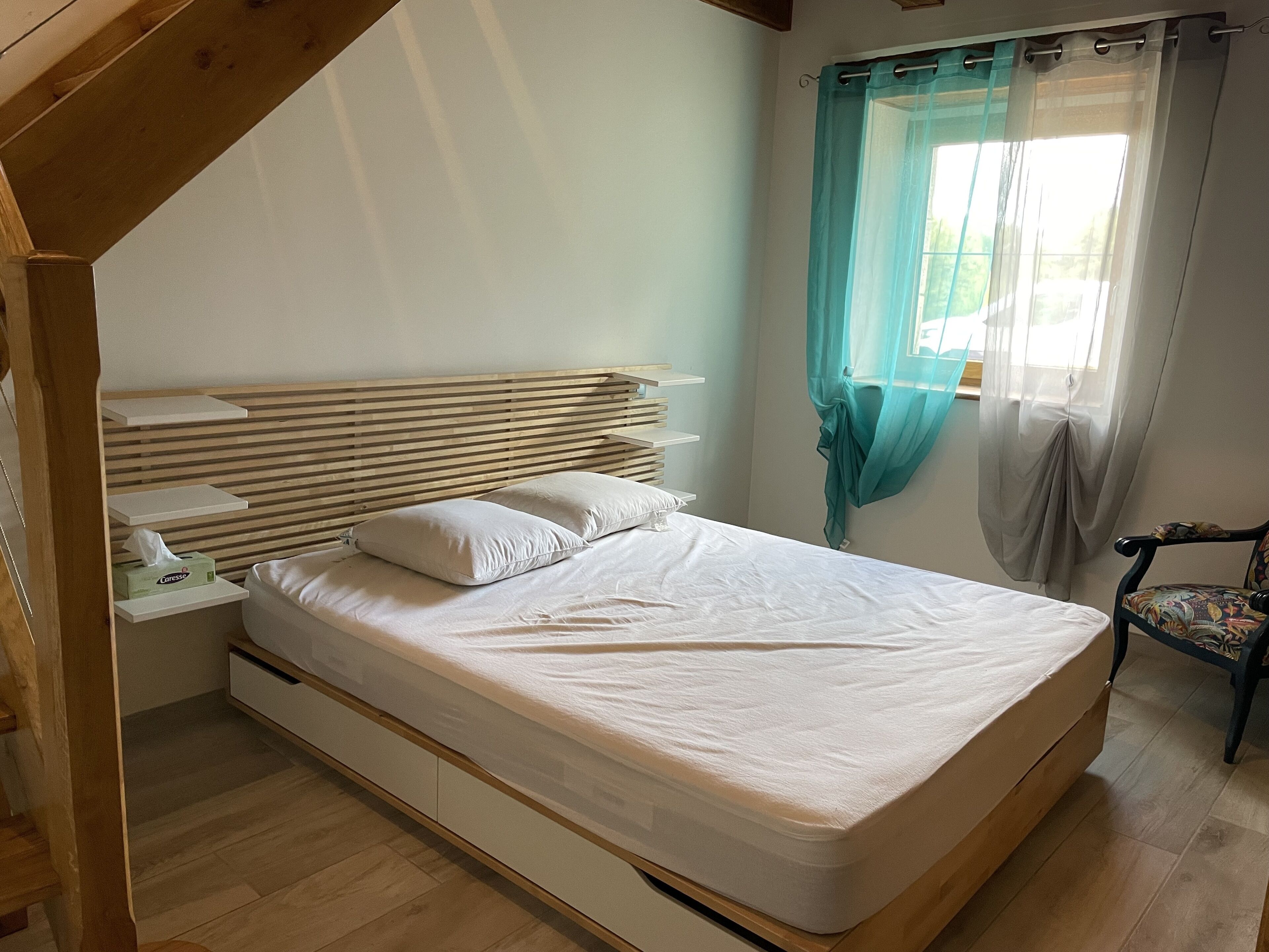 Un dormitorio con cabecera de madera, una cama individual con ropa de cama blanca, una mesita de noche con lámpara y una silla.