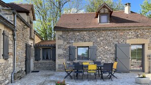 A stone building with a tiled roof, a stone staircase, and a patio area with a table and chairs. - le Gite de Cayla (SAINT-PROJET)