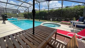 A pool area with a wooden table and lounge chairs under a canopy.