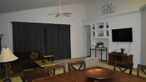 A living room with a dining table, a sofa, a TV, and a ceiling fan.