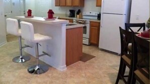A kitchen with wooden cabinets, a white refrigerator, a stove, and two white bar stools.