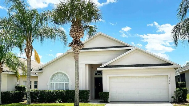 A single-story house with a garage, a front lawn, and palm trees.