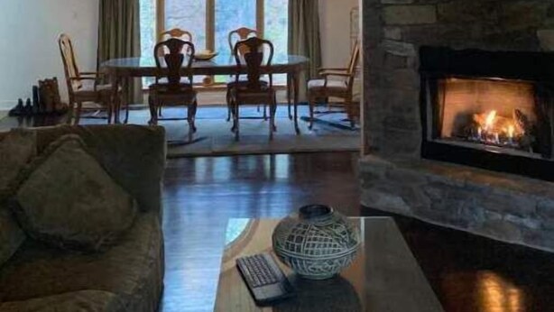 A cozy living room with a stone fireplace, wooden ceiling, and a dining area with chairs and a table.