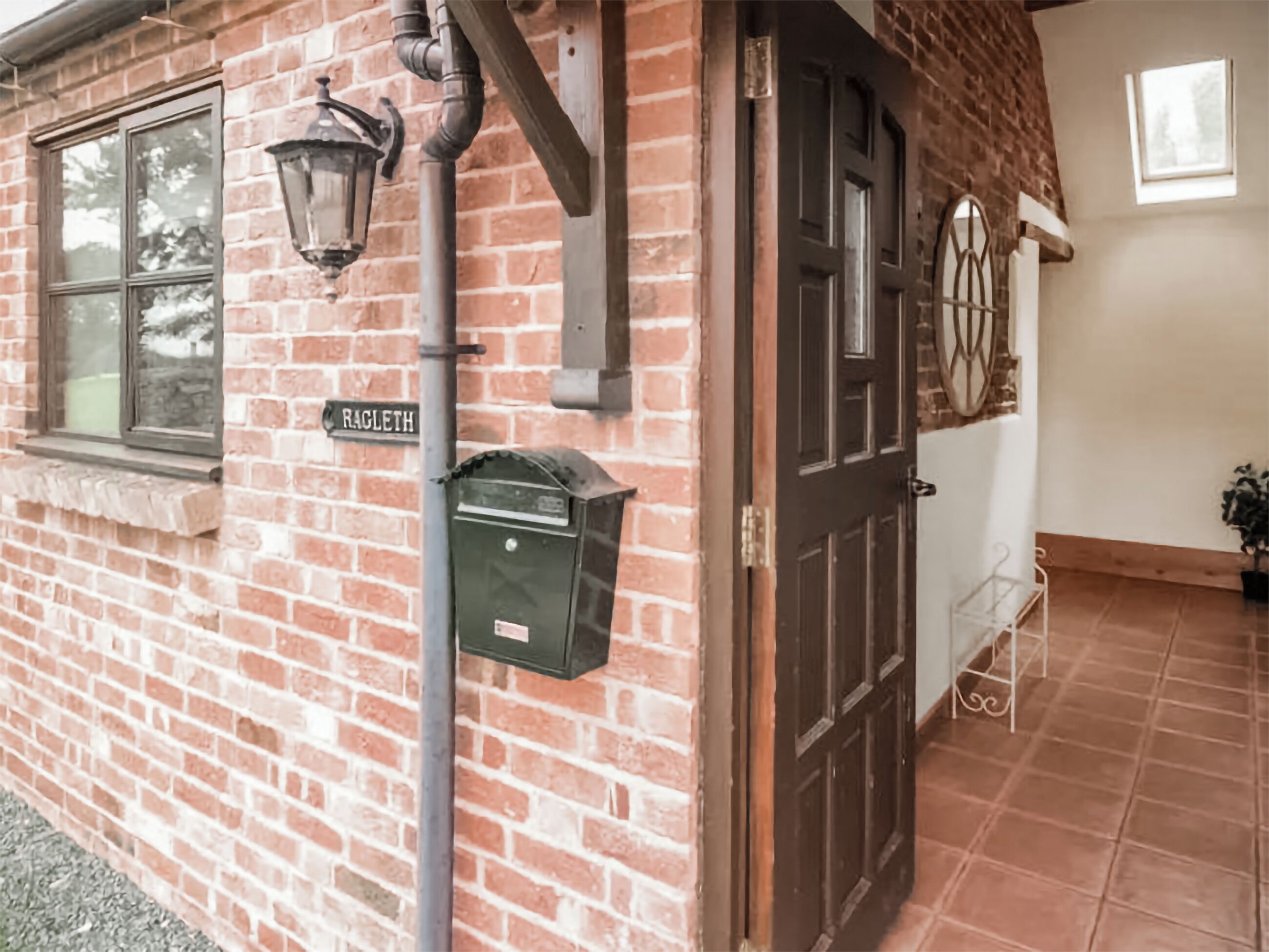 A brick building with a sign reading "RACLETH," a metal door, a window, and a wall-mounted light fixture.