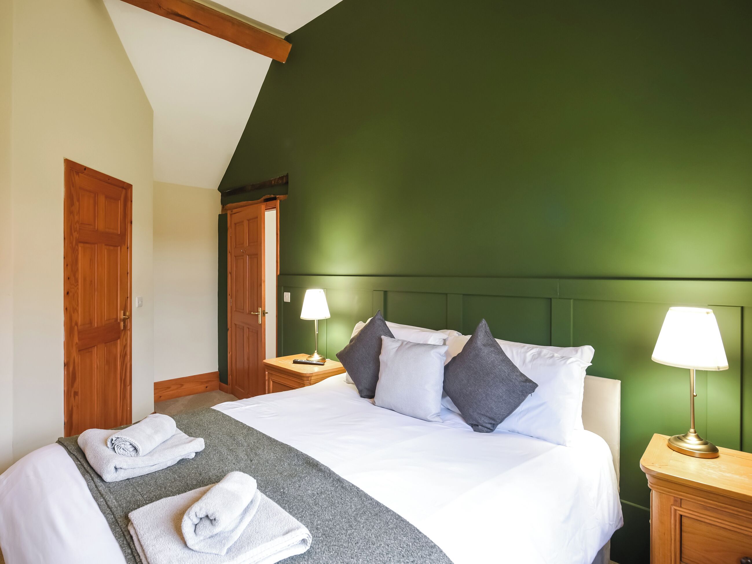 A neatly made bed with pillows and a blanket, two bedside lamps, and a wooden nightstand.