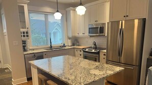 A modern kitchen with white cabinets, stainless steel appliances, and a marble island. - Qualicum Family Cottage - 3bd/2 bath (Qualicum Beach)