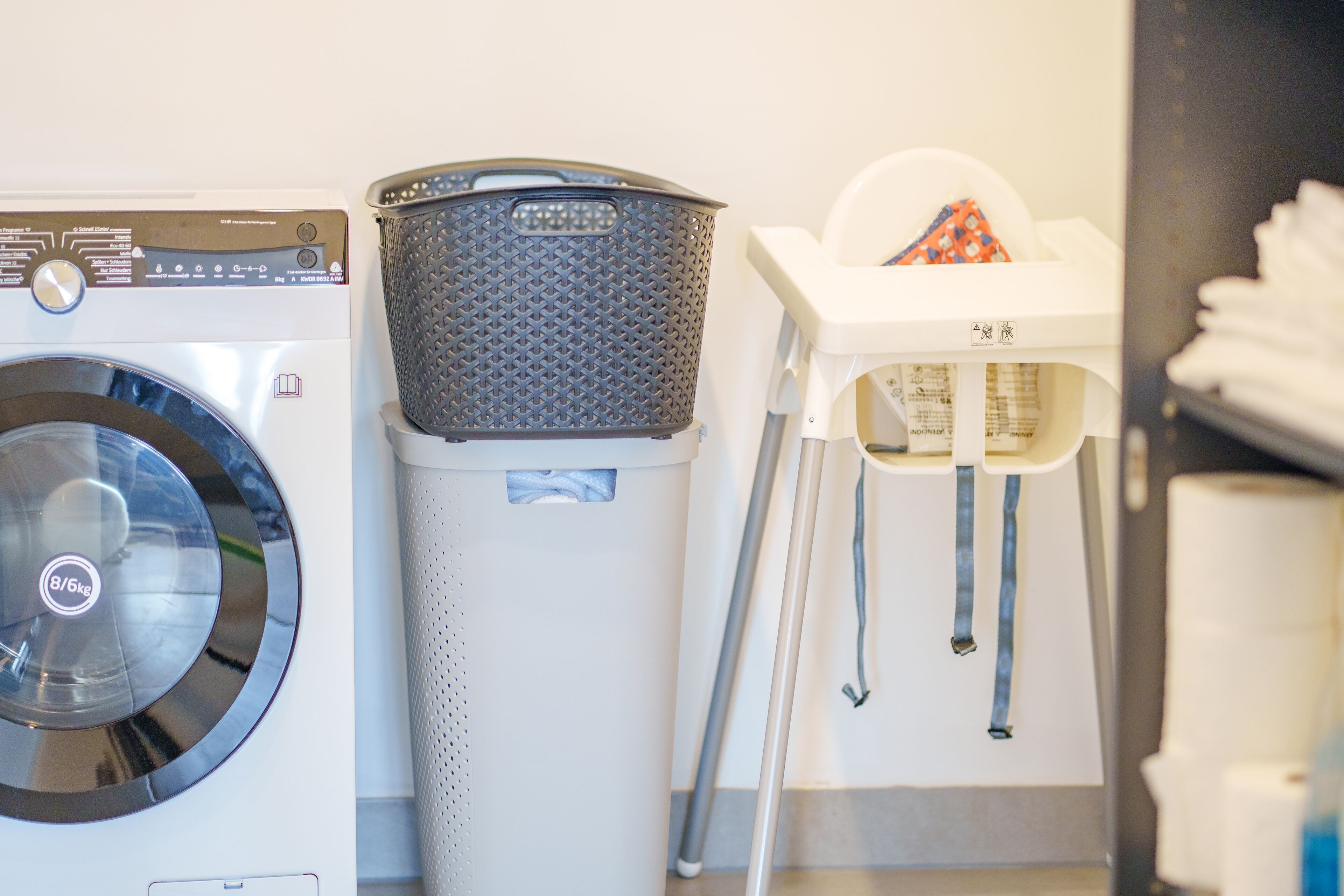 Un espace buanderie comprenant un lave-linge à chargement frontal, une poubelle et un seau à couches.