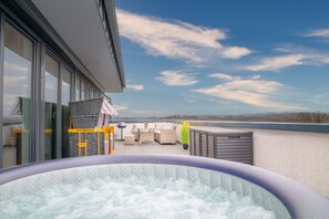 Ein Whirlpool auf einer Dachterrasse mit Gartenmöbeln und Blick zum Himmel.
