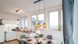Une cuisine moderne avec des meubles blancs, un coin repas doté d’une table en bois pour quatre personnes, et des luminaires suspendus au-dessus.