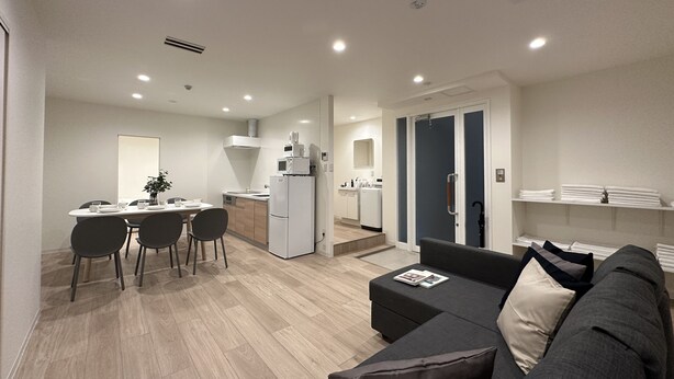 A modern living room with a sofa, a dining area with chairs and a table, a kitchen with appliances, and a door leading to another room. - Nikke 201 (Hiroshima)