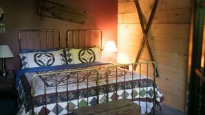 A bedroom with two metal beds, a wooden wall, and a single lamp. - Stowe Austrian Chalet (Waterbury)