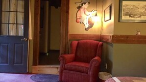 A room with a wooden door, a red armchair, a wall-mounted light fixture, and a framed picture. - Hunger Mountain - Grunberg Haus Inn & Cabins (Waterbury)