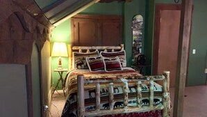 A rustic bedroom with a wooden bed, green walls, and a small table with a lamp. - Green Mountain - Grunberg Haus Inn & Cabins (Waterbury)