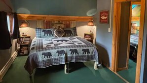 Une chambre confortable avec une tête de lit en bois, une couvre-lit matelassé orné de motifs d’ours, deux lampes de chevet et un miroir au mur.