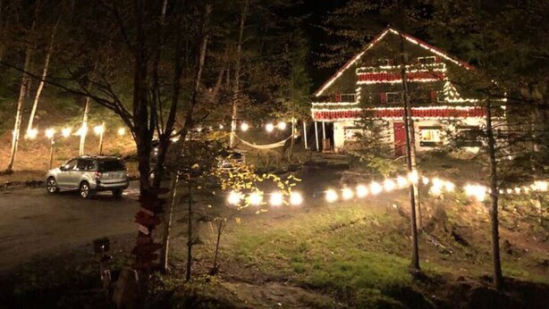 Un bâtiment avec un toit rouge et des murs blancs, entouré d’arbres et illuminé par des guirlandes lumineuses.