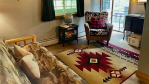 A cozy living room with a sofa, a patterned rug, a chair, a small table with a globe, and a window with curtains.