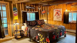 Une pièce chaleureuse, avec des murs en bois, comprenant un lit, une table de chevet, une lampe et une fenêtre.