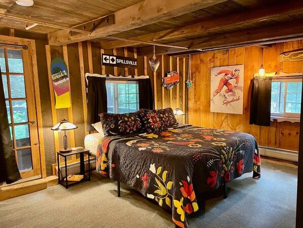 A cozy wooden room with a bed, a nightstand, a lamp, and a window.