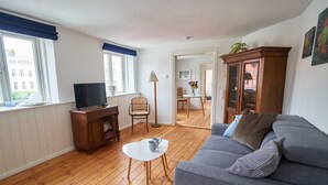 Un salon avec un canapé gris, un meuble en bois, une télévision et une petite table sur laquelle sont posées des tasses.