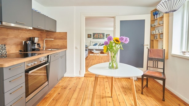 Une cuisine moderne dotée d’un plan de travail en bois, d’appareils électroménagers en acier inoxydable et d’une table à manger blanche agrémentée d’un vase de fleurs.